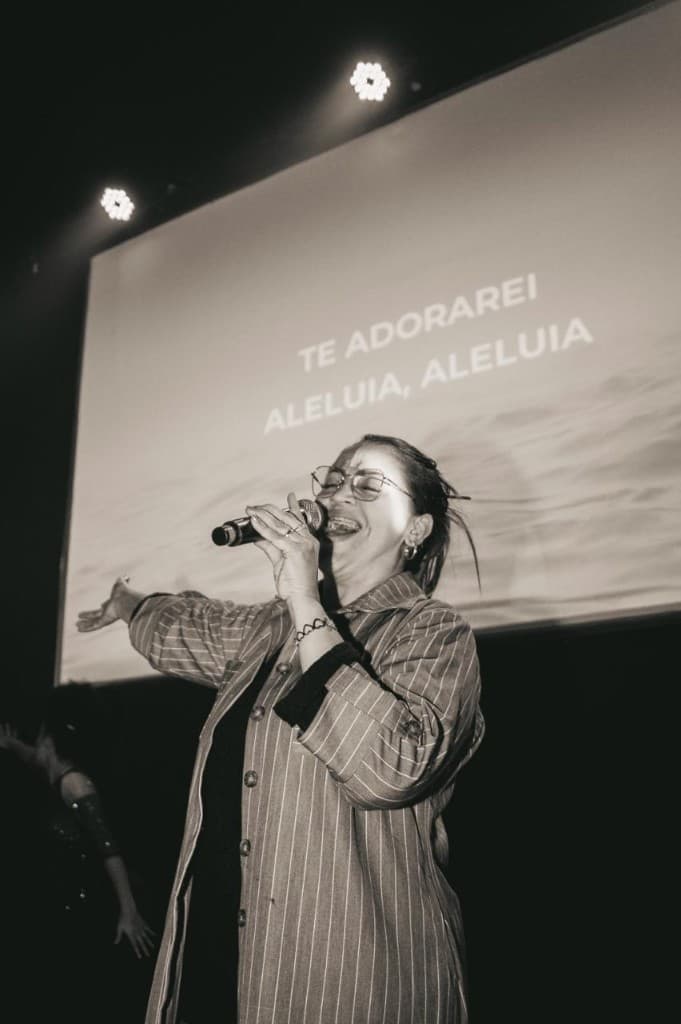 Sheylla Rodrigues cantando no palco, com a projeção Te Adorarei, Aleluia ao fundo