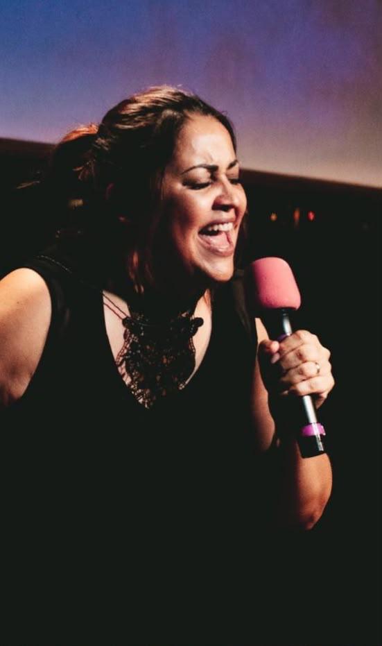 Sheylla Rodrigues cantando, com um microfone rosa